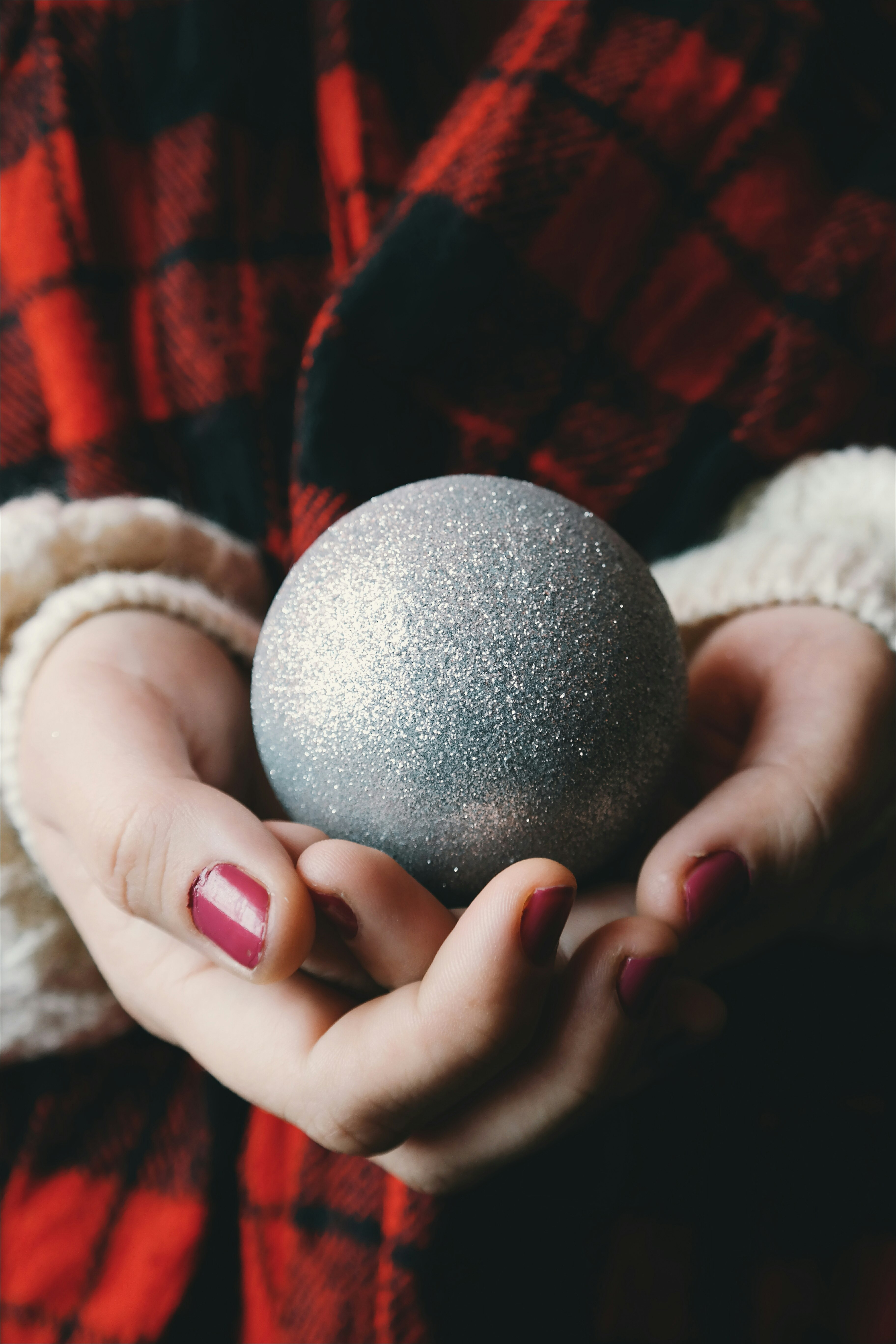 A woman with red painted nails holding a silver Christmas ornament.